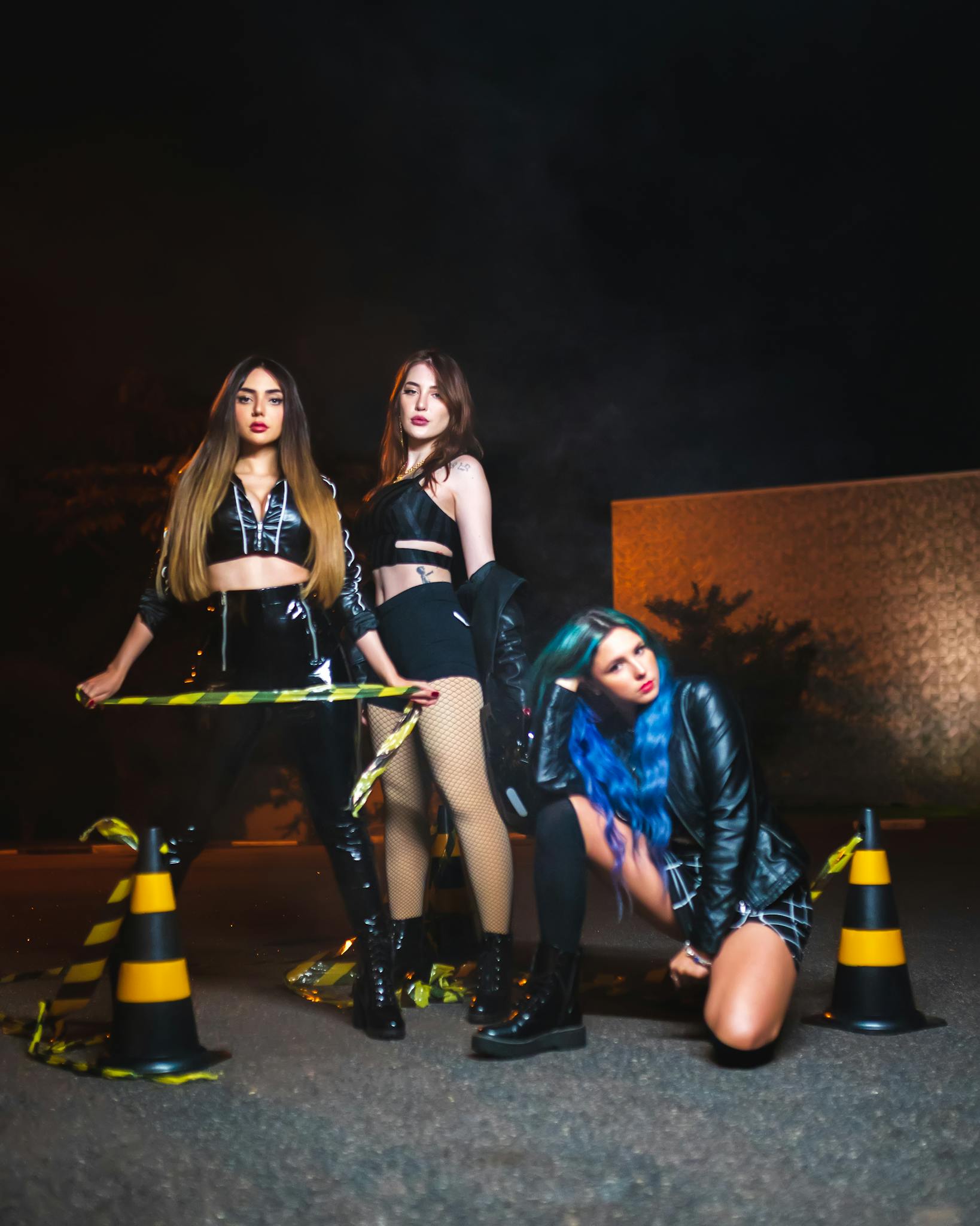 Vibrant fashion photography of three young women posing on a nighttime street with traffic cones.