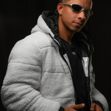 Fashion portrait of a young man in a fluffy hoodie and sunglasses on a black background.