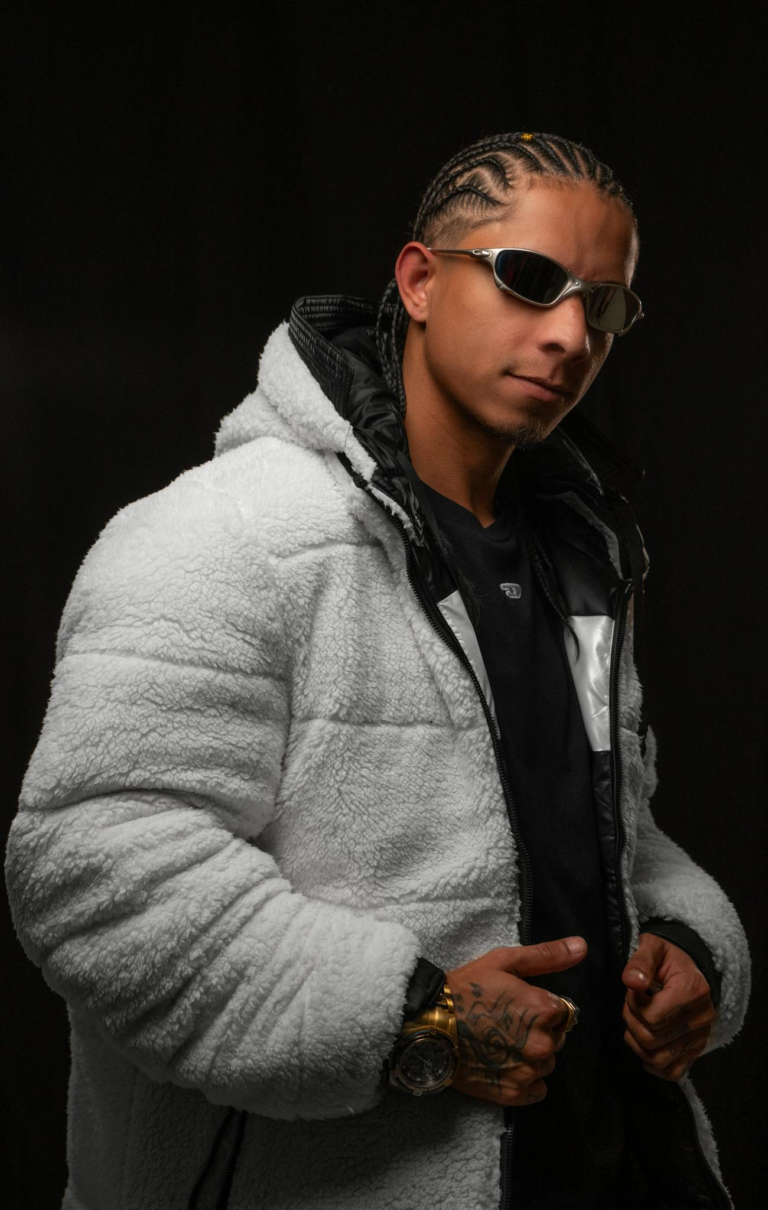 Fashion portrait of a young man in a fluffy hoodie and sunglasses on a black background.